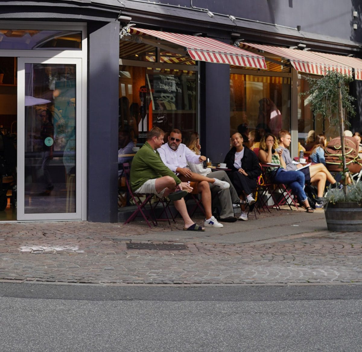 Street terrace with guests seated under striped awnings outside a SHOUT Media coffee shop
